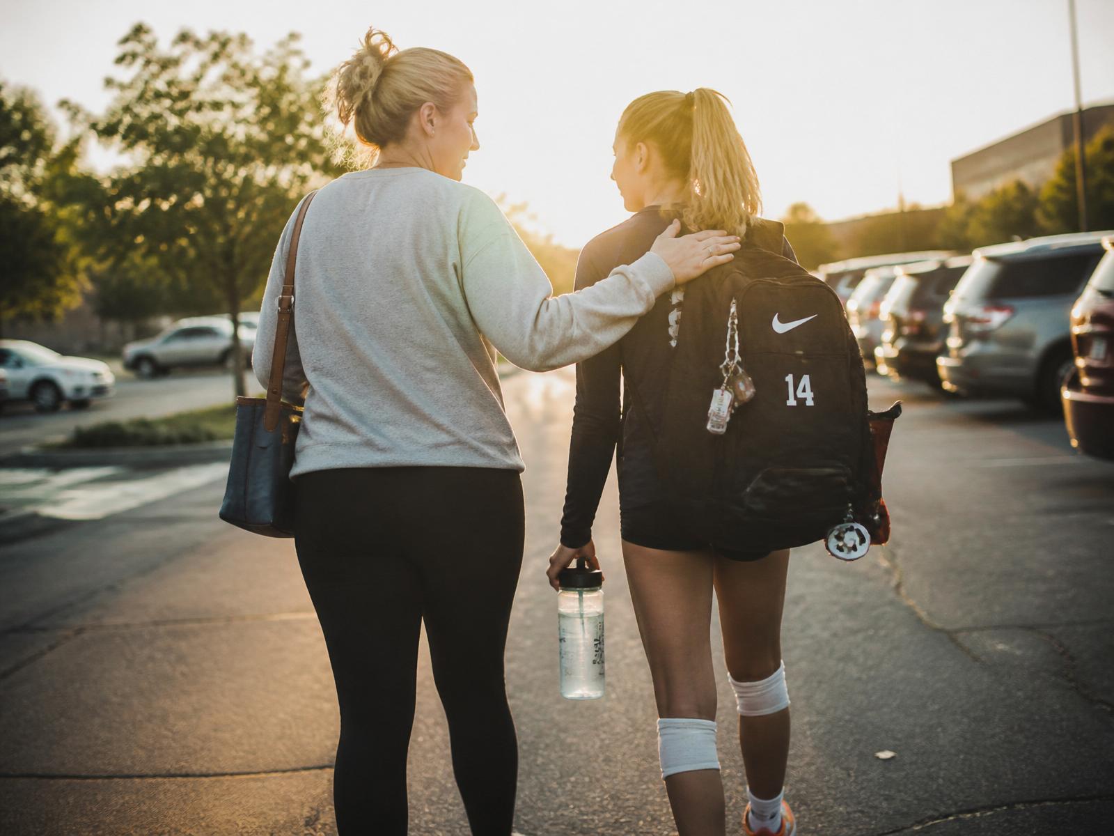 A Black mother and her teenage daughter walking together on a track after volleyball practice, laughing in conversation