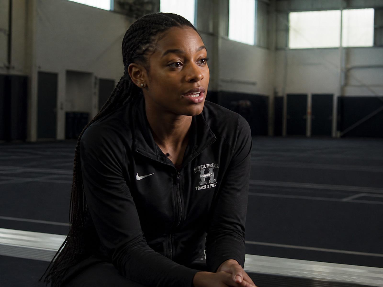 Female track athlete being interviewed inside an empty field house, mid-sentence