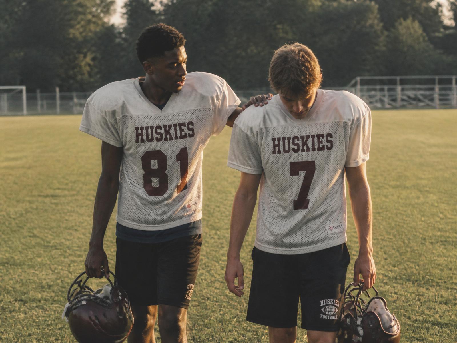 One football player with hand on a teammate's shoulder walking off the field at golden hour