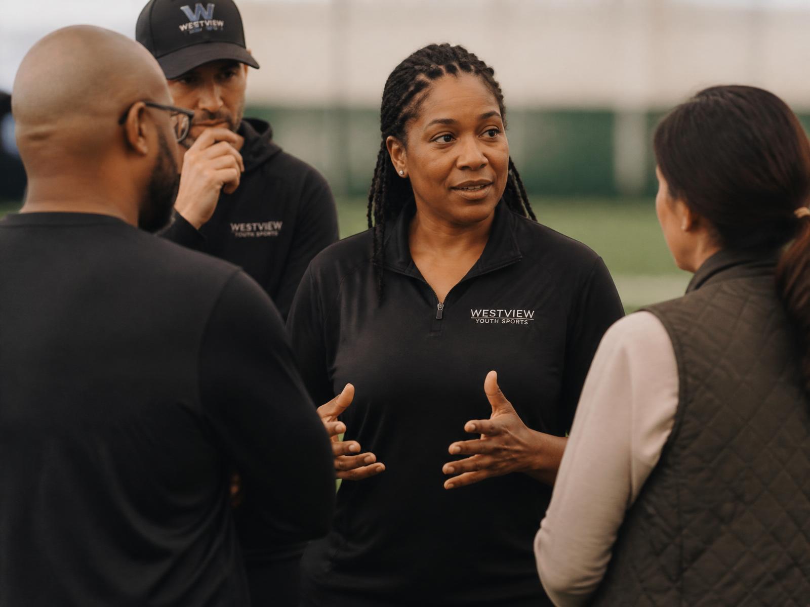 Club director in collaborative conversation with two coaches and a parent inside a training facility